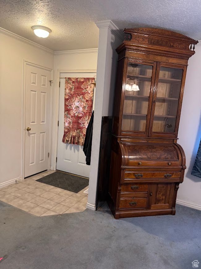 Carpeted entrance foyer featuring a textured ceiling, ornamental molding, baseboards, and tile patterned flooring | Image 18
