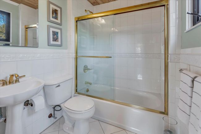Bathroom with toilet, tile patterned flooring, tile walls, and combined bath / shower with glass door | Image 17