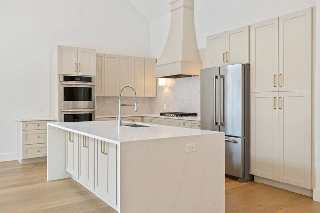Kitchen with stainless steel appliances, custom exhaust hood, decorative backsplash, a sink, and light wood-style floors | Image 11