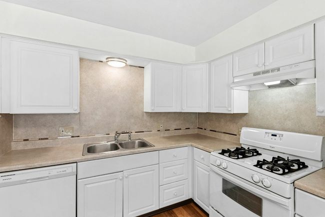 Kitchen featuring white appliances, under cabinet range hood, white cabinets, and light countertops | Image 9