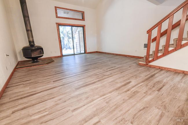 Unfurnished living room featuring wood finished floors, a wood stove, and a towering ceiling | Image 12