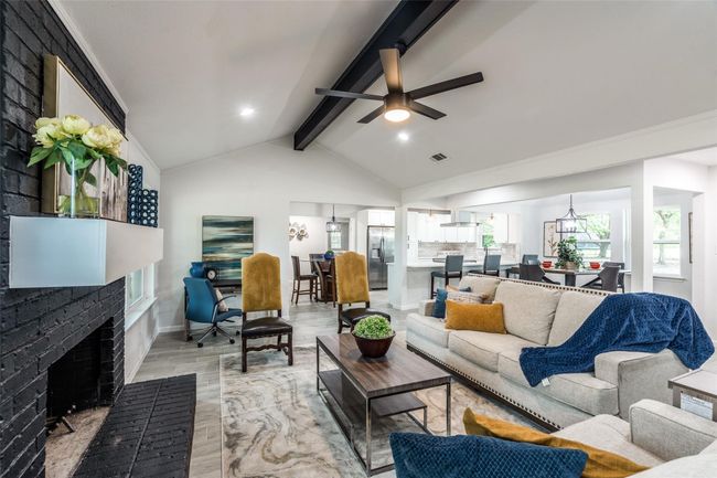 Living area featuring beam ceiling, a fireplace, wood finished floors, a ceiling fan, and high vaulted ceiling | Image 4