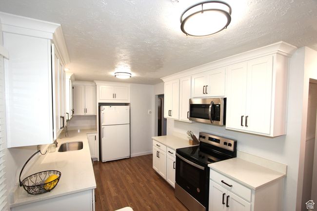 Kitchen with appliances with stainless steel finishes, white cabinetry, dark wood-style flooring, light countertops, and a textured ceiling | Image 12