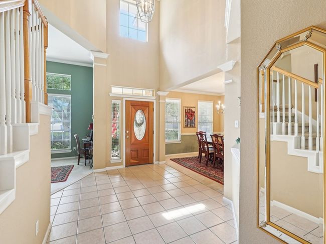 Entrance foyer featuring a towering ceiling, a chandelier, stairway, light tile patterned flooring, and baseboards | Image 4