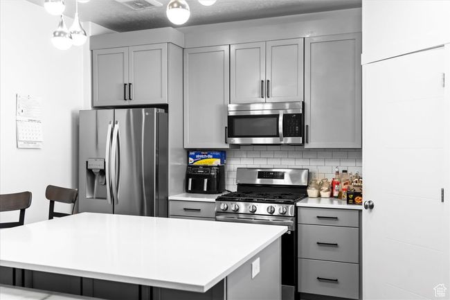 Kitchen with decorative backsplash, gray cabinets, light countertops, a kitchen island, and appliances with stainless steel finishes | Image 8