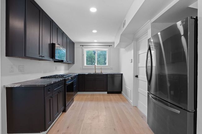 Kitchen featuring appliances with stainless steel finishes, light wood-style flooring, recessed lighting, dark stone counters, and dark cabinetry | Image 10