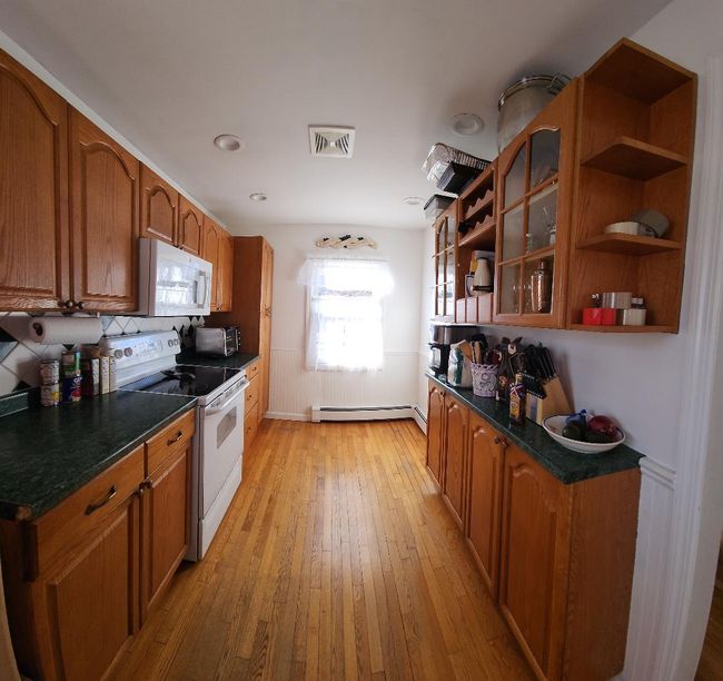 Kitchen featuring a wainscoted wall, visible vents, white appliances, brown cabinets, and open shelves | Image 4