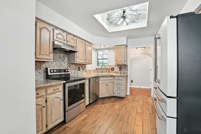 Kitchen featuring stainless steel appliances, under cabinet range hood, ceiling fan, decorative backsplash, and light wood finished floors | Image 9