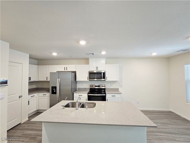 Kitchen featuring stainless steel appliances, a sink, white cabinetry, light wood-type flooring, and light stone countertops | Image 10