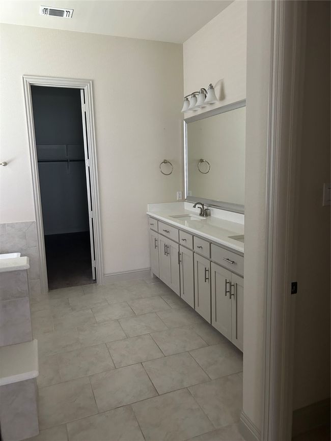 Full bathroom featuring double vanity, a walk in closet, and a tub to relax in | Image 9