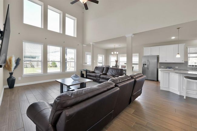 This open floor plan connects the Living Room, Dining, and Kitchen. Floor to ceiling windows provide impressive natural light and show off the dramatic ceiling height. | Image 12