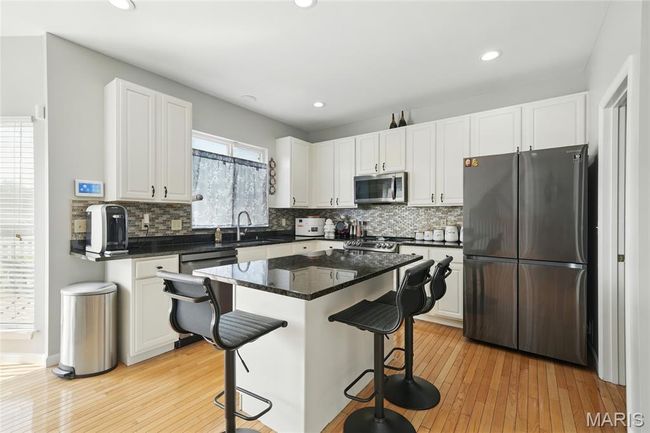 Kitchen with stainless steel appliances, a breakfast bar area, tasteful backsplash, white cabinetry, and recessed lighting | Image 11