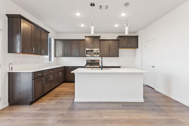 Kitchen with visible vents, light wood-style floors, appliances with stainless steel finishes, decorative backsplash, and dark brown cabinets | Image 6