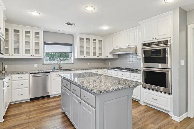 Kitchen with visible vents, wood finished floors, stainless steel appliances, under cabinet range hood, and a sink | Image 7