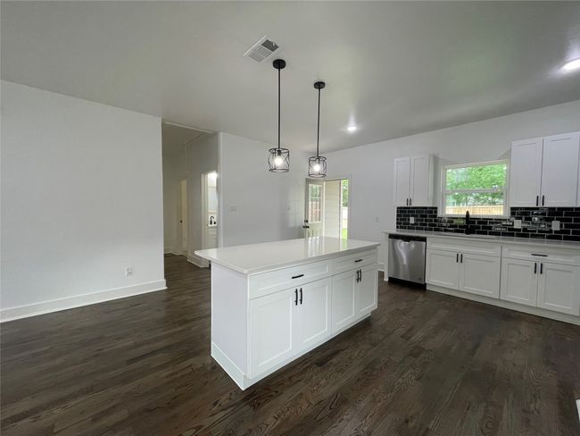 Kitchen with stainless steel dishwasher, dark wood-type flooring, backsplash, a sink, and a center island | Image 21