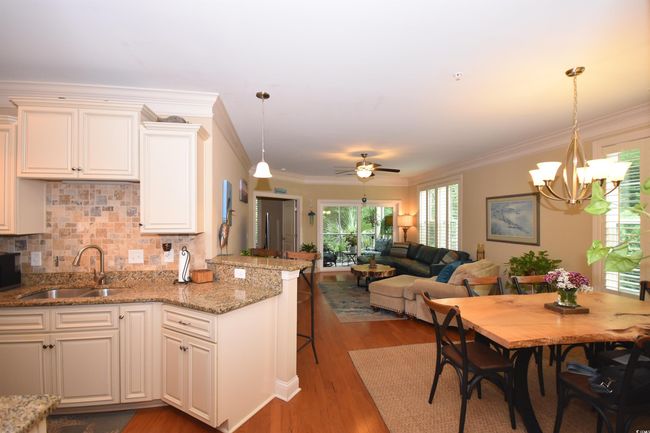 Kitchen featuring wood finished floors, light stone counters, a peninsula, ceiling fan, and backsplash | Image 12