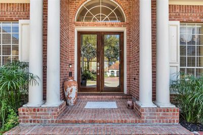 Check out the elegant entrance featuring a stately door with glass panels, framed by four classic white columns under an arched transom, and flanked by lush greenery and decorative pottery. (pottery is a peronal item) | Image 3