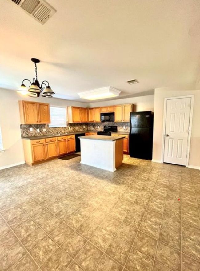 Kitchen with black appliances, decorative backsplash, a chandelier, hanging light fixtures, and baseboards | Image 5