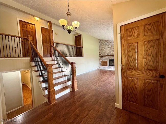 Staircase with a textured ceiling, wood-type flooring, an inviting chandelier, vaulted ceiling, and a brick fireplace | Image 11