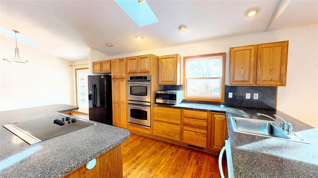 Kitchen with light wood-style flooring, a sink, black appliances, dark countertops, and tasteful backsplash | Image 10