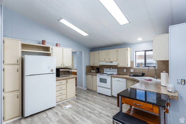 Kitchen with white appliances, vaulted ceiling, under cabinet range hood, a sink, and light wood finished floors | Image 7