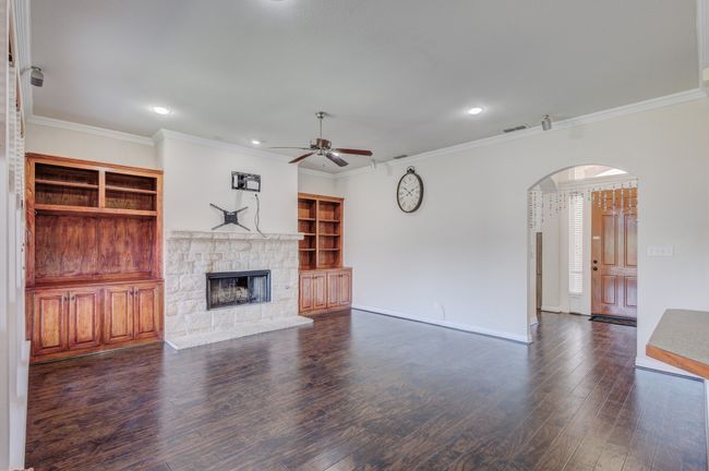 Unfurnished living room featuring dark wood-type flooring, built in features, crown molding, and a stone fireplace | Image 20