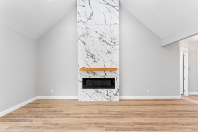 Unfurnished living room with high vaulted ceiling, baseboards, a fireplace, and wood finished floors | Image 8