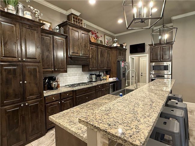 Kitchen with crown molding, a chandelier, a kitchen breakfast bar, decorative backsplash, and appliances with stainless steel finishes | Image 8