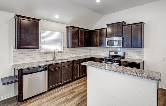 Kitchen featuring appliances with stainless steel finishes, light wood-style floors, vaulted ceiling, light stone counters, and recessed lighting | Image 29