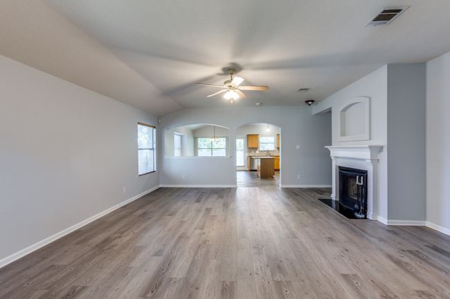 Unfurnished living room featuring ceiling fan, wood finished floors, a fireplace, arched walkways, and vaulted ceiling | Image 7