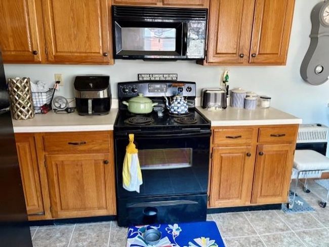 Kitchen with light countertops, black appliances, and brown cabinetry | Image 17