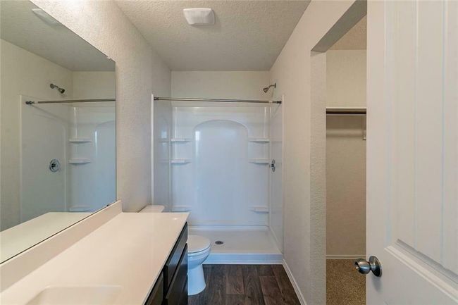 Bathroom featuring walk in shower, wood finished floors, a textured ceiling, vanity, and a textured wall | Image 10