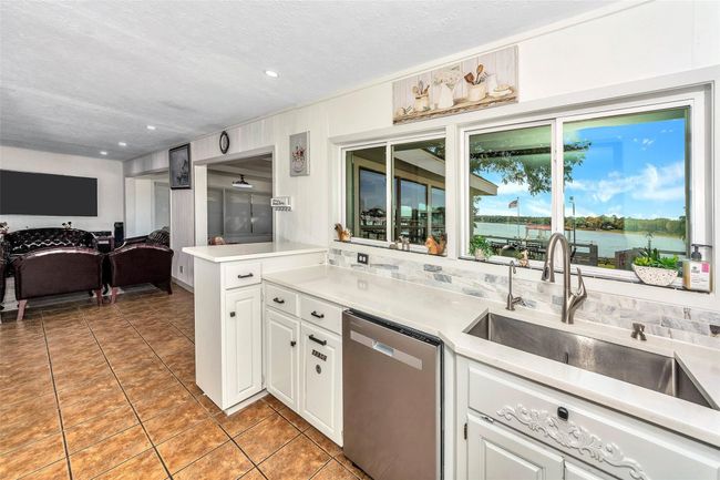 Kitchen featuring stainless steel dishwasher, a sink, light tile patterned floors, white cabinetry, and light countertops | Image 13