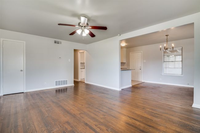 Unfurnished living room featuring visible vents, ceiling fan with notable chandelier, baseboards, and dark wood-style floors | Image 7