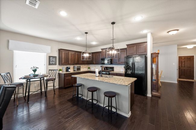 Kitchen with dark brown cabinetry, recessed lighting, an island with sink, visible vents, and black appliances | Image 16