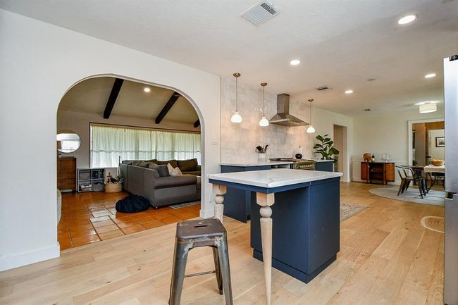 This open-concept home features a modern kitchen with an island, stylish pendant lighting, and a cozy living area with exposed beams. The space is bright with wood and tile flooring, creating a warm and inviting atmosphere. | Image 19