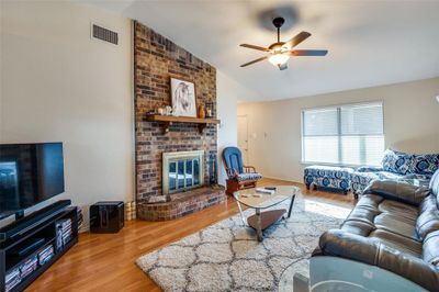 Living room featuring vaulted ceiling, hardwood / wood-style floors, ceiling fan, and a brick fireplace | Image 2