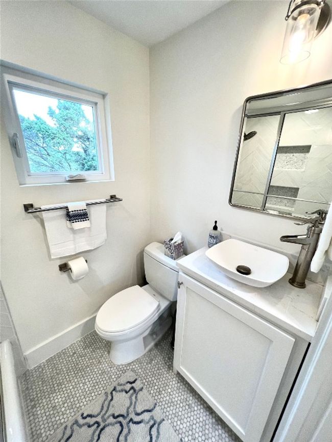 Sleek and modern hall bath with stylish fixtures, a chic vessel sink, and natural light from a window with a charming view. | Image 14