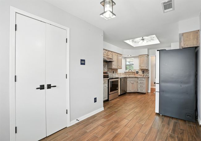 Kitchen with stainless steel appliances, a skylight, wood finished floors, light countertops, and tasteful backsplash | Image 12