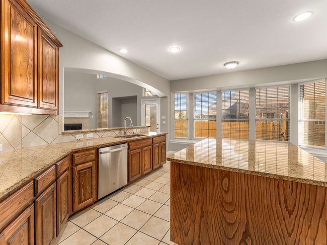 Kitchen featuring light tile patterned floors, brown cabinetry, a sink, dishwasher, and backsplash | Image 16