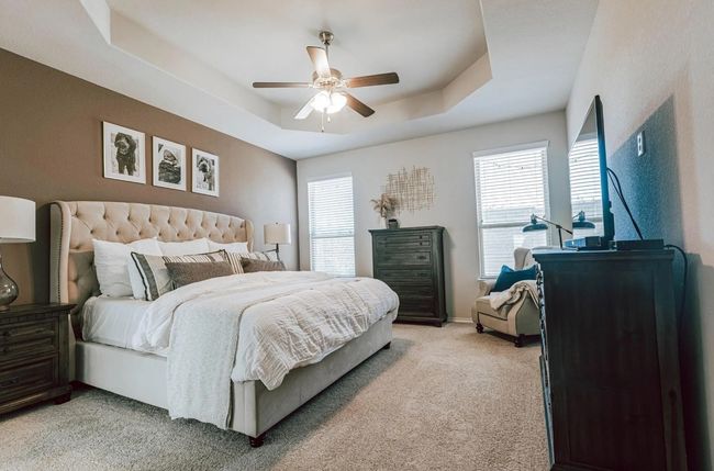 Bedroom featuring multiple windows, a raised ceiling, a ceiling fan, and light colored carpet | Image 24
