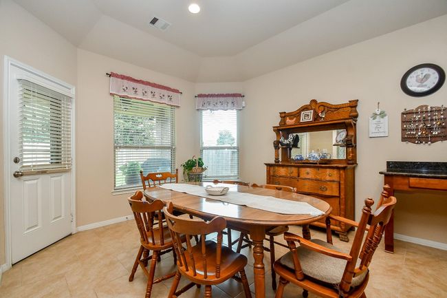 The dining area features a cozy, traditional design with a wooden table and chairs, an antique-style sideboard, and ample natural light from large windows. | Image 14