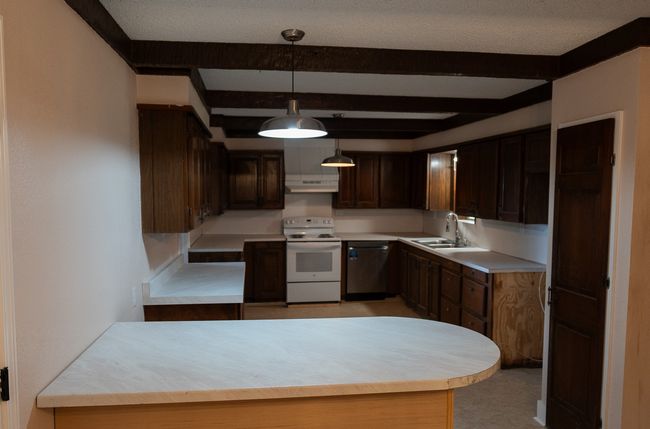 Kitchen with white range with electric cooktop, stainless steel dishwasher, extractor fan, beam ceiling, and light countertops | Image 11