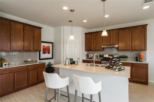 Kitchen featuring stainless steel range, backsplash, light countertops, under cabinet range hood, and a breakfast bar area | Image 10