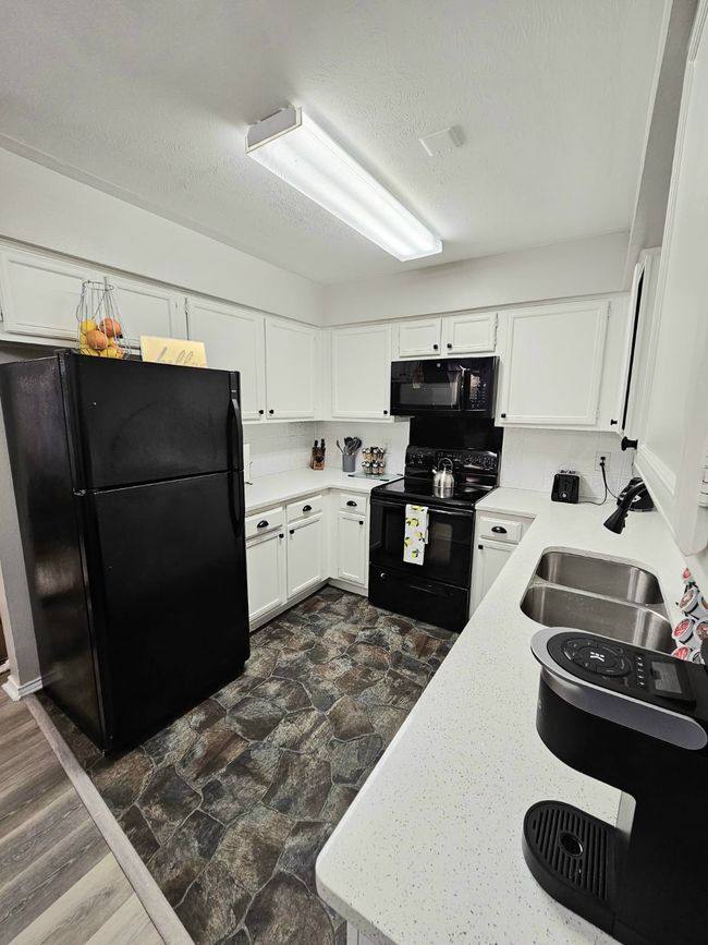 Kitchen with black appliances, light countertops, dark stone finish flooring, white cabinetry, and a textured ceiling | Image 14