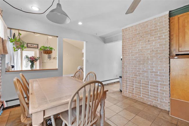 Dining space featuring light tile patterned floors, brick wall, a baseboard heating unit, and ceiling fan | Image 6