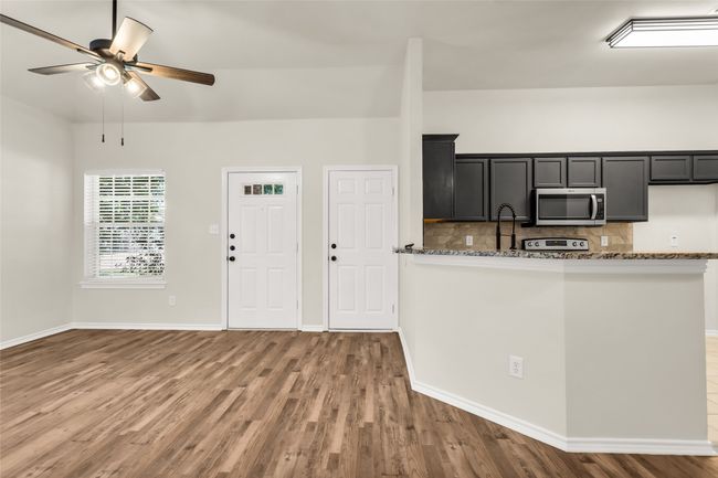 Kitchen featuring decorative backsplash, light stone countertops, stainless steel microwave, dark cabinetry, and a ceiling fan | Image 6