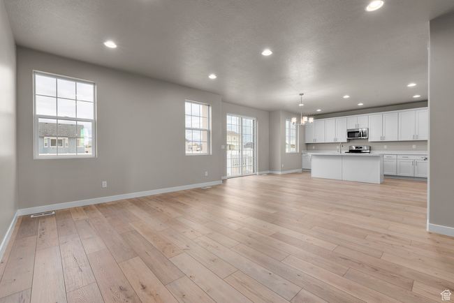 Unfurnished living room with baseboards, a chandelier, a sink, light wood-type flooring, and recessed lighting | Image 8