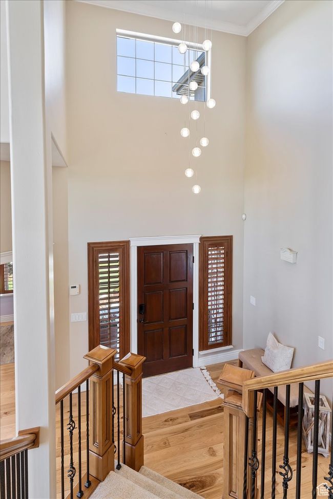 Foyer entrance featuring crown molding, an inviting chandelier, wood finished floors, and a towering ceiling | Image 4