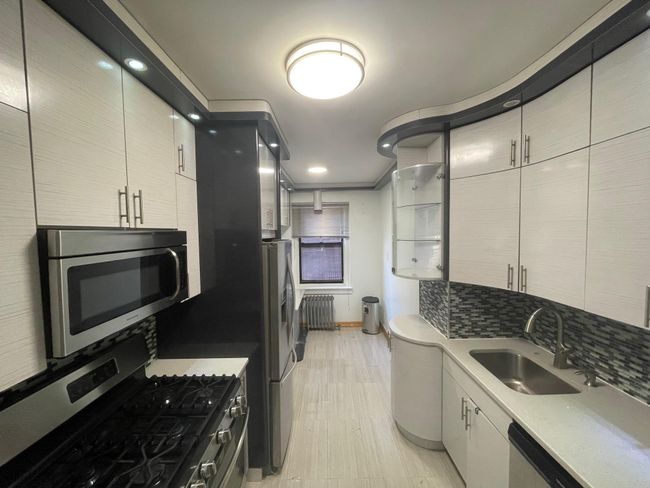 Kitchen featuring radiator heating unit, a sink, stainless steel appliances, backsplash, and baseboards | Image 4